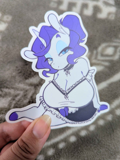 Sticker of an animated character with purple hair held by a hand on a textured surface.